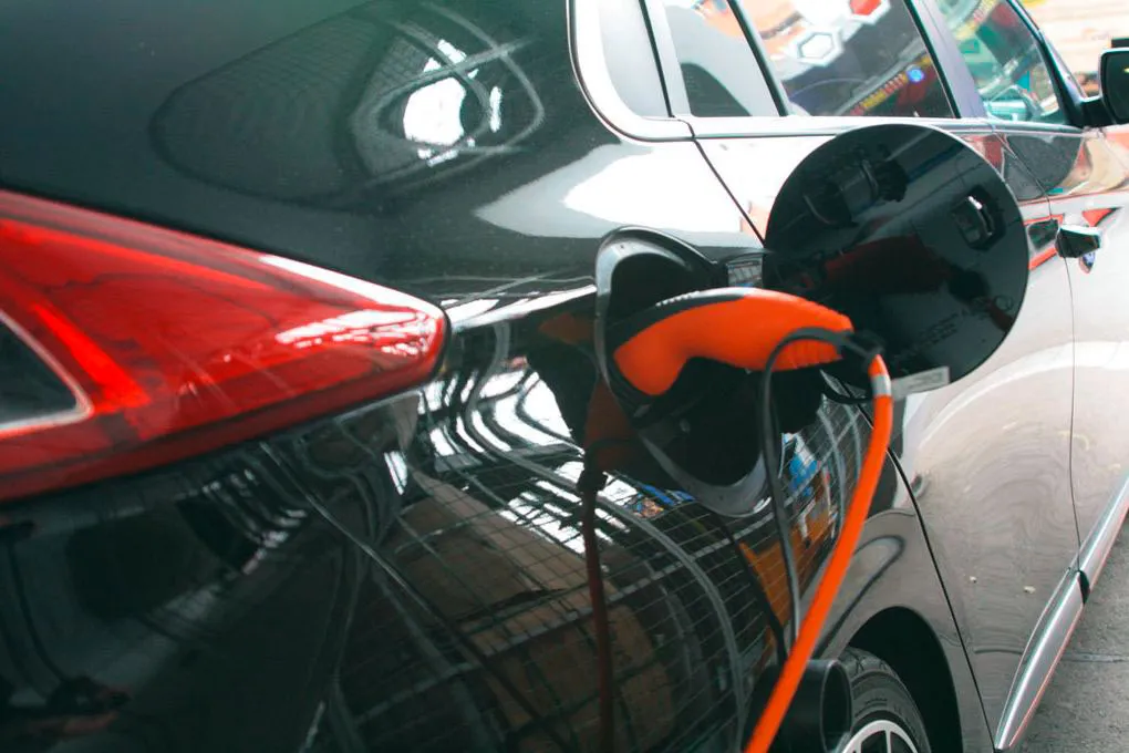 Nahaufnahme eines Elektrofahrzeugs beim Aufladen, mit dem orangefarbenen Ladekabel, das an den Ladeanschluss des Fahrzeugs angeschlossen ist.