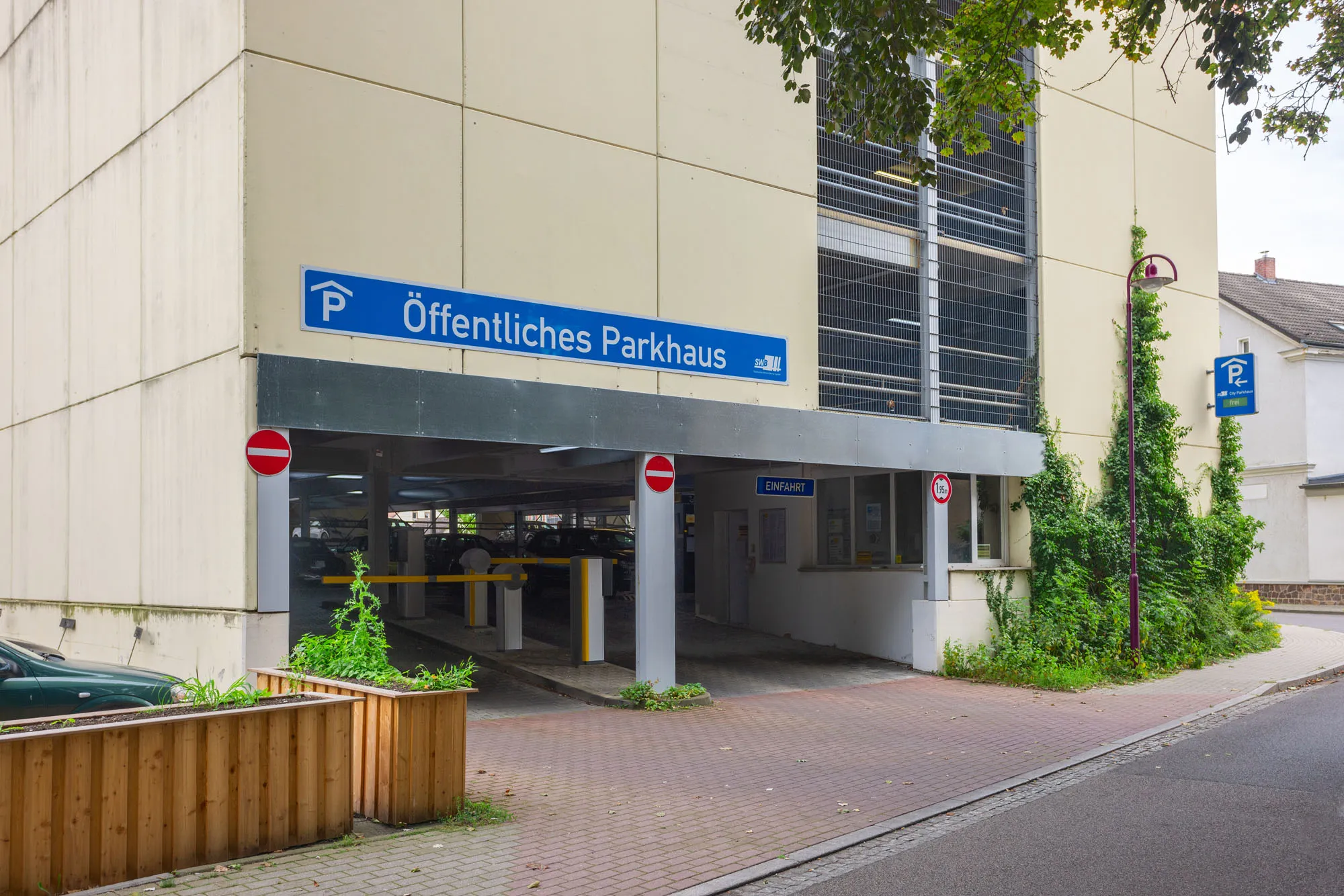 Das Bild zeigt die Einfahrt zu einem mehrstöckigen öffentlichen Parkhaus mit der Aufschrift Öffentliches Parkhaus und mehreren Verbotsschildern an der Fassade.