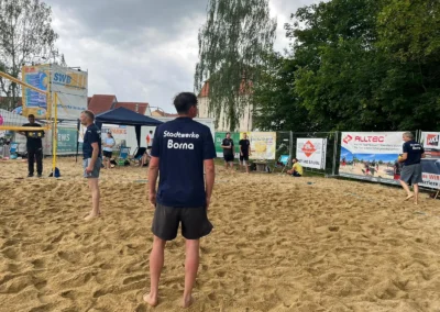 Vier Personen stehen auf einem sandigen Volleyballfeld im Freien, sie tragen passende Trikots der Stadtwerke Borna, im Hintergrund sind Bäume und Banner zu sehen.
