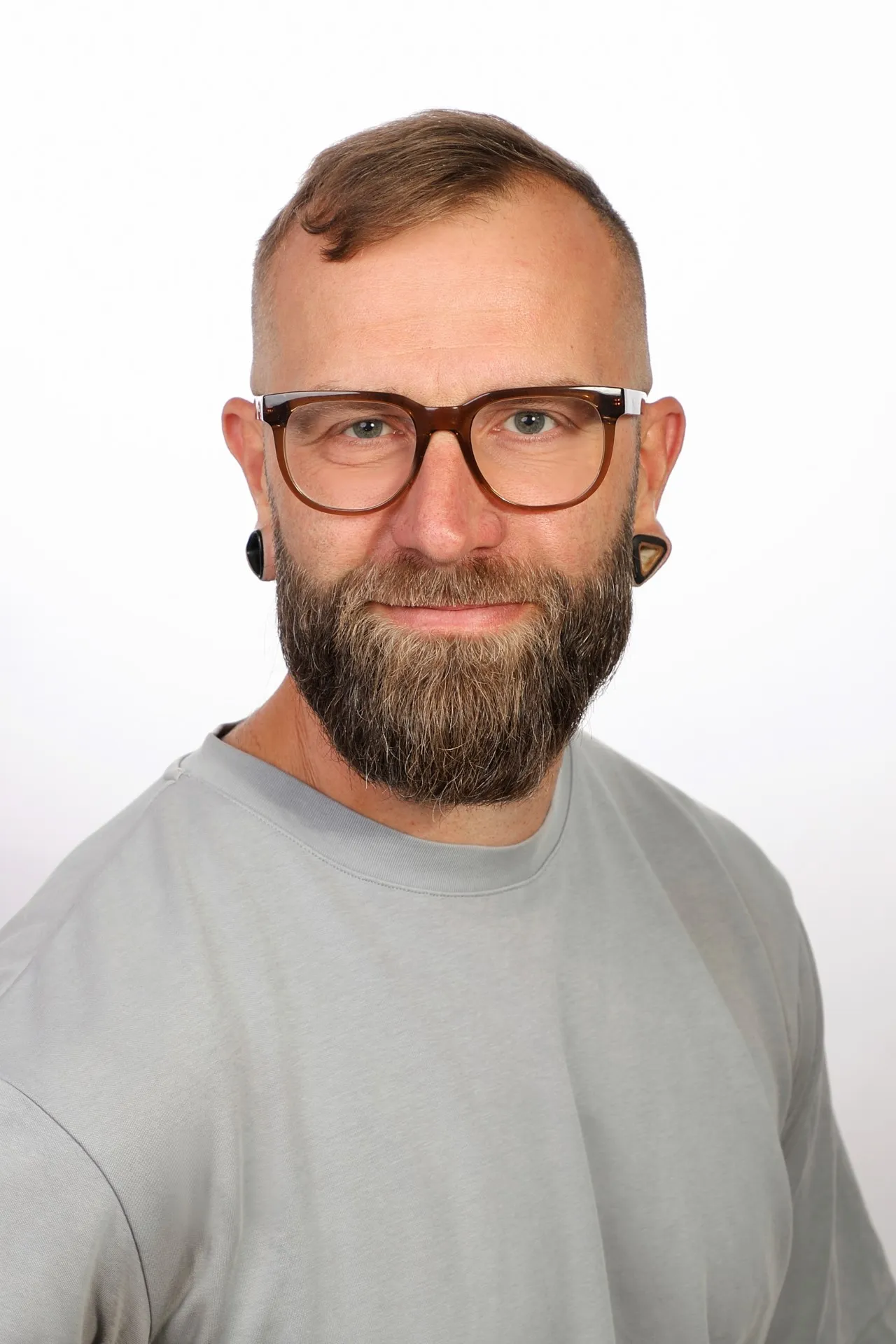 Ein Mann mit Bart und Brille, der ein graues T-Shirt trägt.